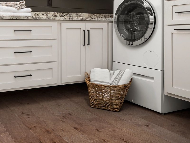 A white laundry basket next to a white washing machine on a brown hardwood floor from Sams Floor Covering in Winchester, KY